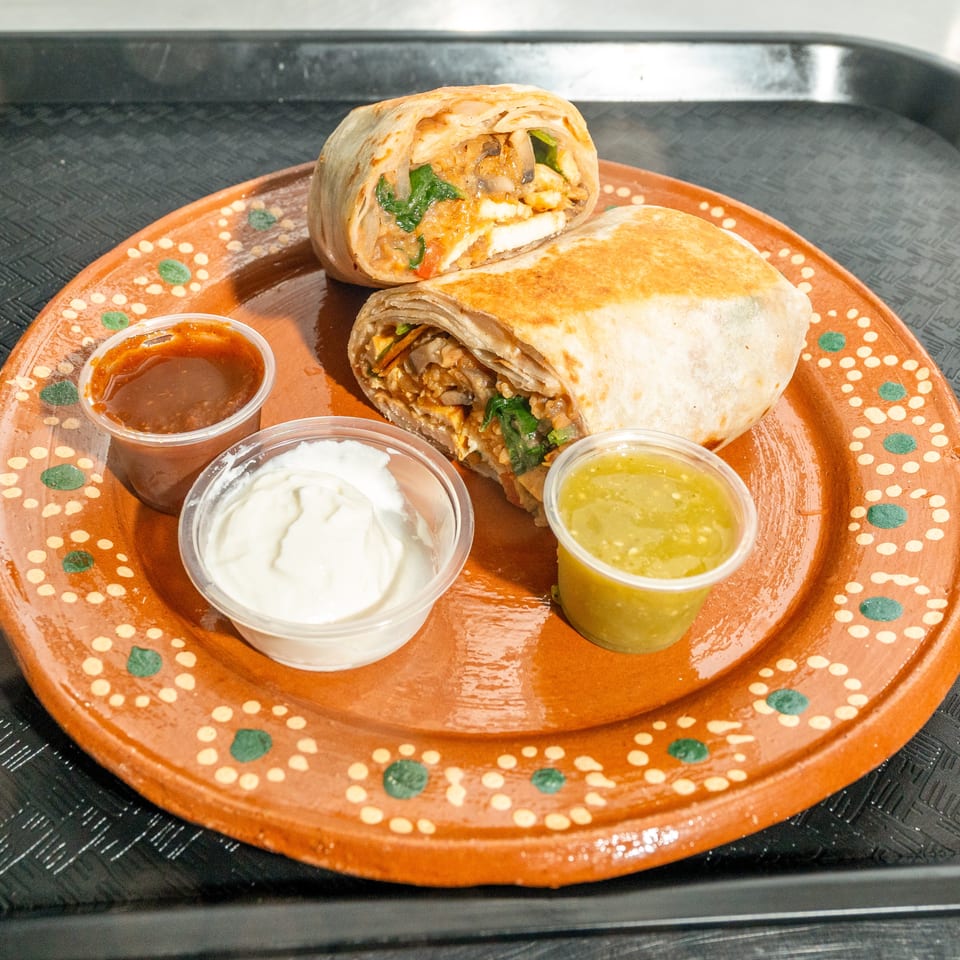 Two burritos, one cut in half, on a decorative brown plate with three dipping sauces.
