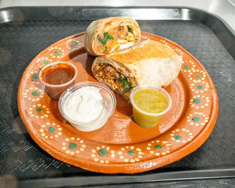 Two burritos, one cut in half, on a decorative brown plate with three dipping sauces.