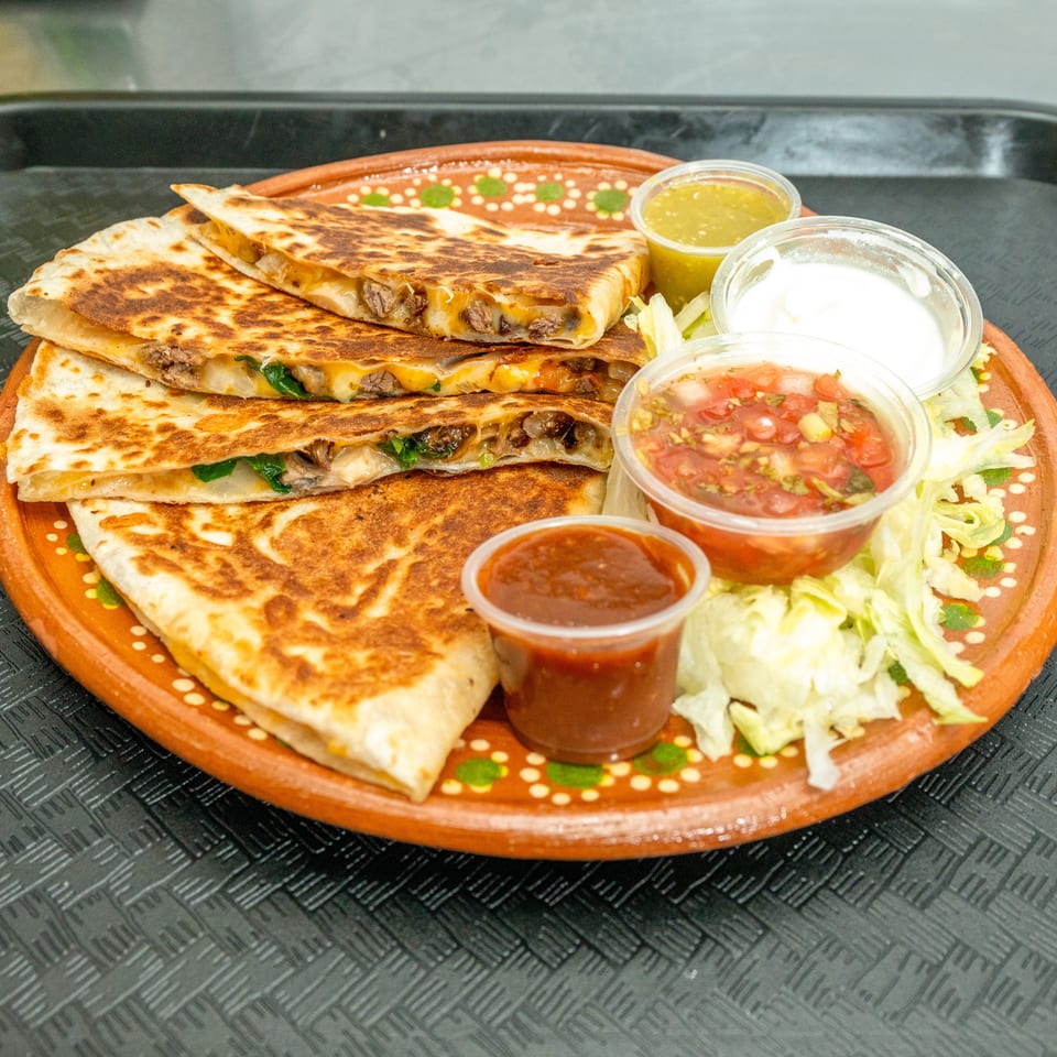 Four quesadilla slices with meat and cheese, served with salsa, sour cream, and shredded lettuce.