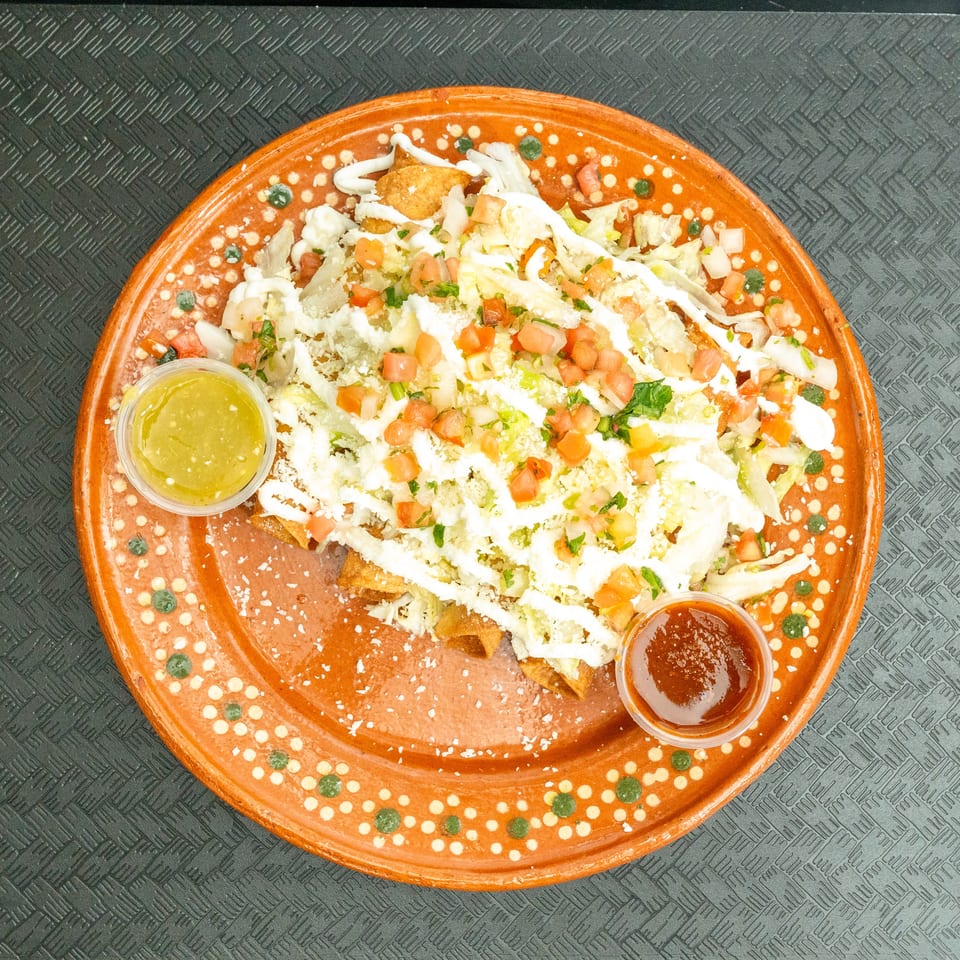 Crispy taquitos topped with shredded lettuce, diced tomatoes, sour cream, and cheese, with two dipping sauces.