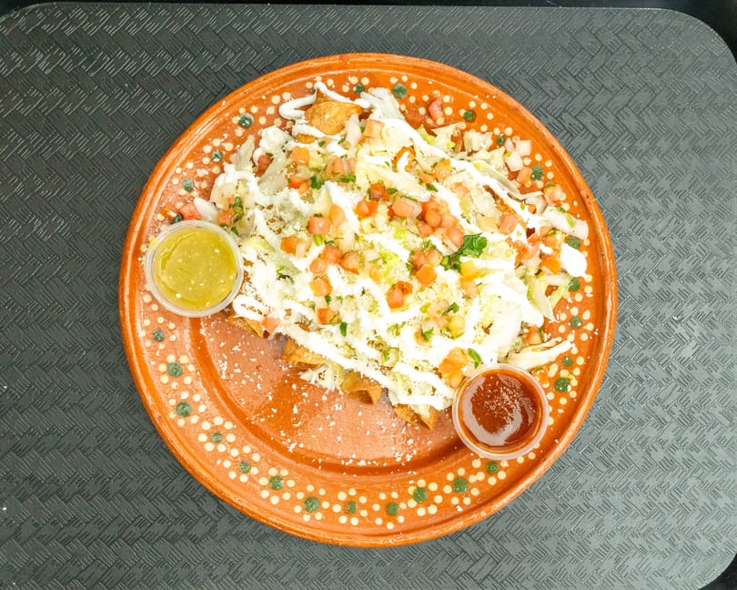 Crispy taquitos topped with shredded lettuce, diced tomatoes, sour cream, and cheese, with two dipping sauces.