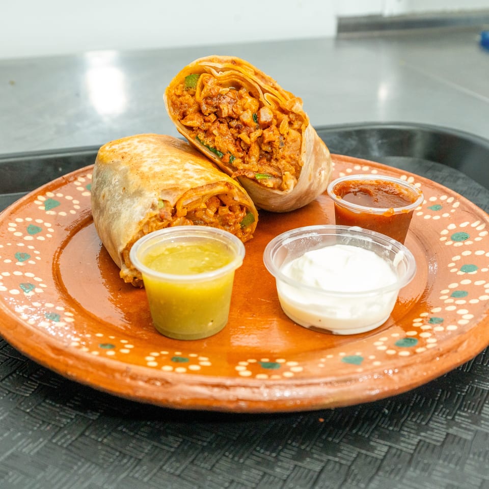 Two burritos, one cut in half, on a decorative orange plate with three dipping sauces.