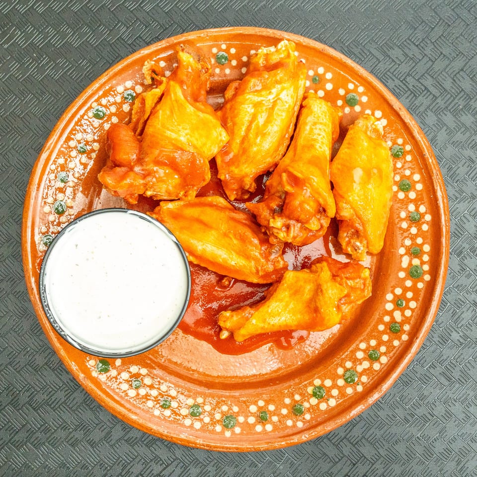 Top-down view of six orange chicken wings with sauce and a side of ranch dressing on a decorative plate.