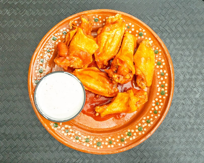 Top-down view of six orange chicken wings with sauce and a side of ranch dressing on a decorative plate.
